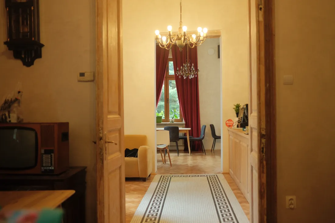 Un salon cu tavan înalt, candelabru și parchet, care se deschide către sufragerie