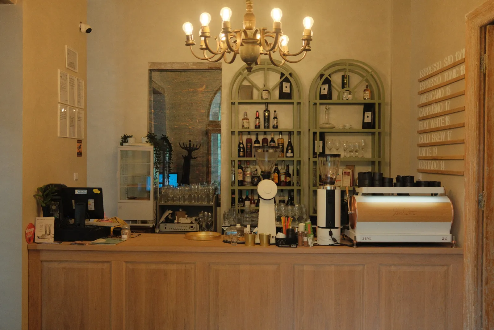 Barul de cafea în întregime, sub un candelabru de alamă, cu rafturile de sticle în spate